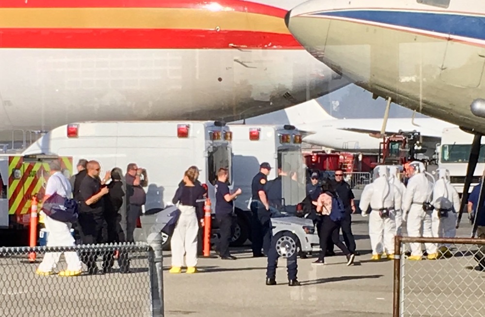 Image of plane and a crowd directly outside, including EMT's, firefighters and men in white hazard suits.